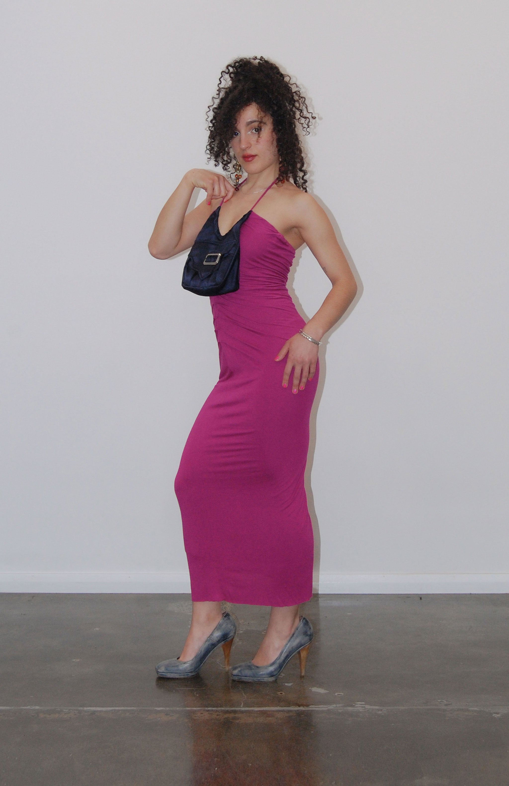 Midi length maxi dress in fuchsia jersey with attached navy purse pocket. Features flattering pleats from underarm to the high hip, thigh high slit and adjustable tie spaghetti strap. Fully lined with square buckle and magnetic button closure on purse.