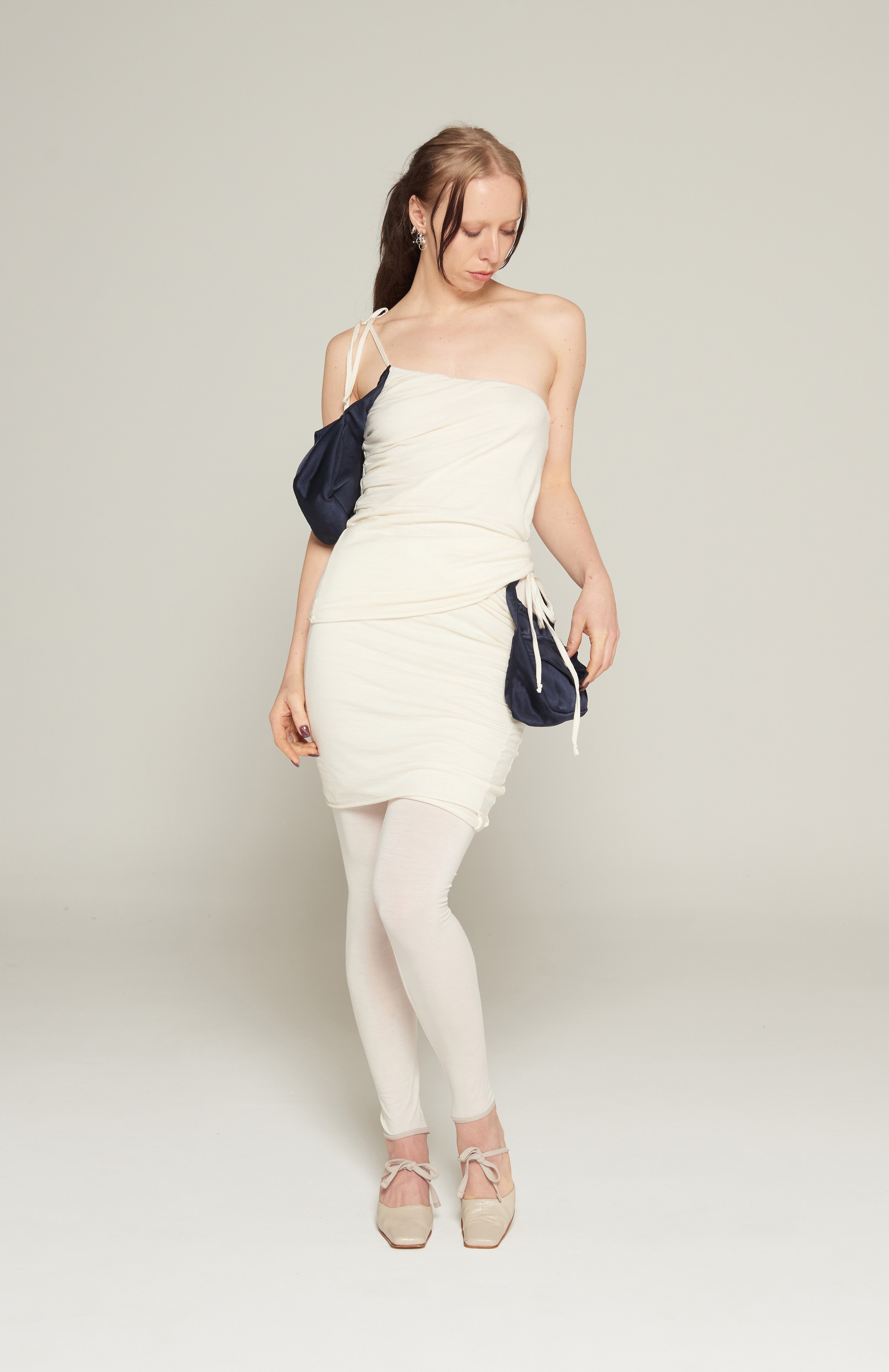 Soft cream wool jersey tank with attached Navy purse pocket. Features, flattering pleats from under arm outer-shell, raw hem and adjustable tie spaghetti strap. fully lined with square buckle and magnetic button.   This purse Tank has been designed to be worn in multiple ways; one with the purse at the underarm, At the front with the straps fashioned as a halter and alternately at the hip worn as a skirt.